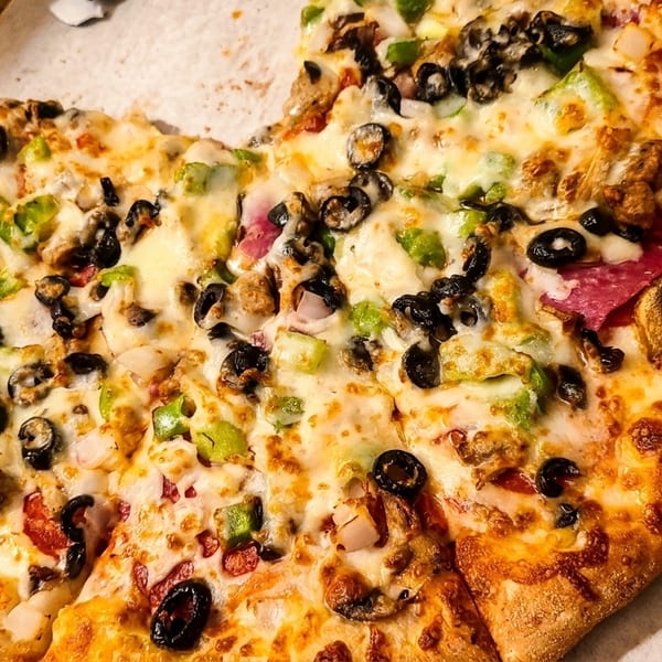 A partially eaten supreme pizza with olives, peppers, and pepperoni in a cardboard box.