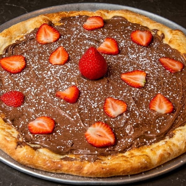 Dessert pizza with Nutella, powdered sugar, and fresh strawberries on a metal pan.