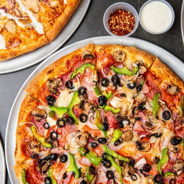 Four pizzas on metal trays, including chicken, supreme, Hawaiian, and a dessert pizza.